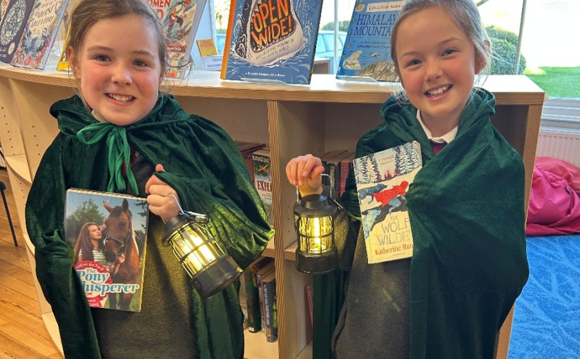two smiling girls holding a book and a lamp
