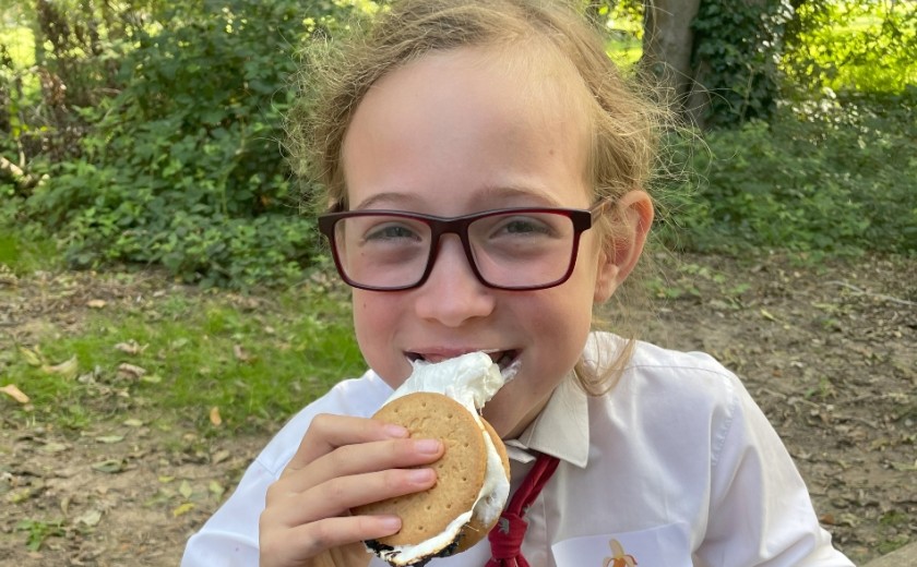 young girl eating a s'more in the woods